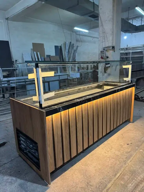 Doğal ahşap dikey panelli, siyah mermer tablalı, amber LED aydınlatmalı ve düz camlı modern çiğköfte soğutma dolabı