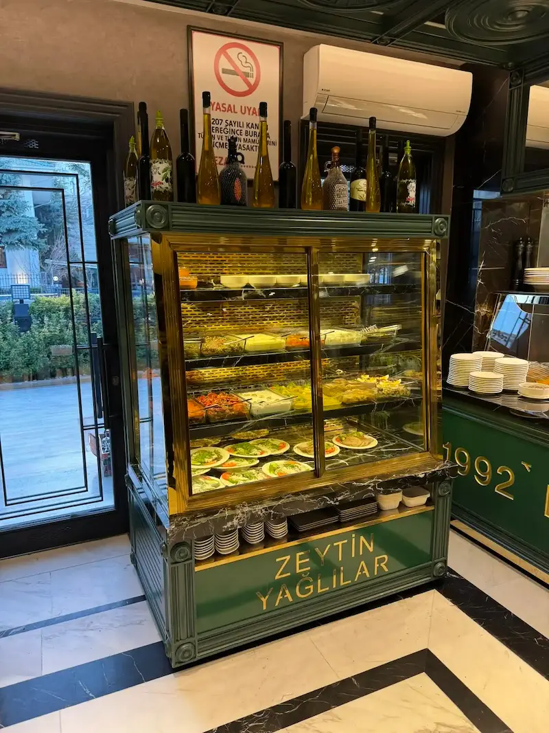 Koyu yeşil lake boyalı, altın varak yazılı ve pirinç çerçeveli, siyah mermer kaideli modern zeytinyağlı ve soğuk mezze teşhir dolabı