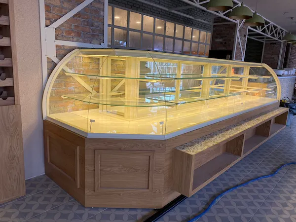 L tipi köşe dönüşlü, açık ahşap kaplamalı, bombeli camlı ve seramik detaylı büyük pastane teşhir reyonu