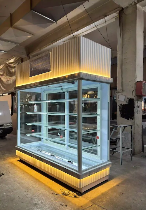 Beyaz oluklu panelli, gold çerçeve detaylı, gün ışığı led aydınlatmalı modern dikey pasta teşhir vitrini ve soğutma dolabı